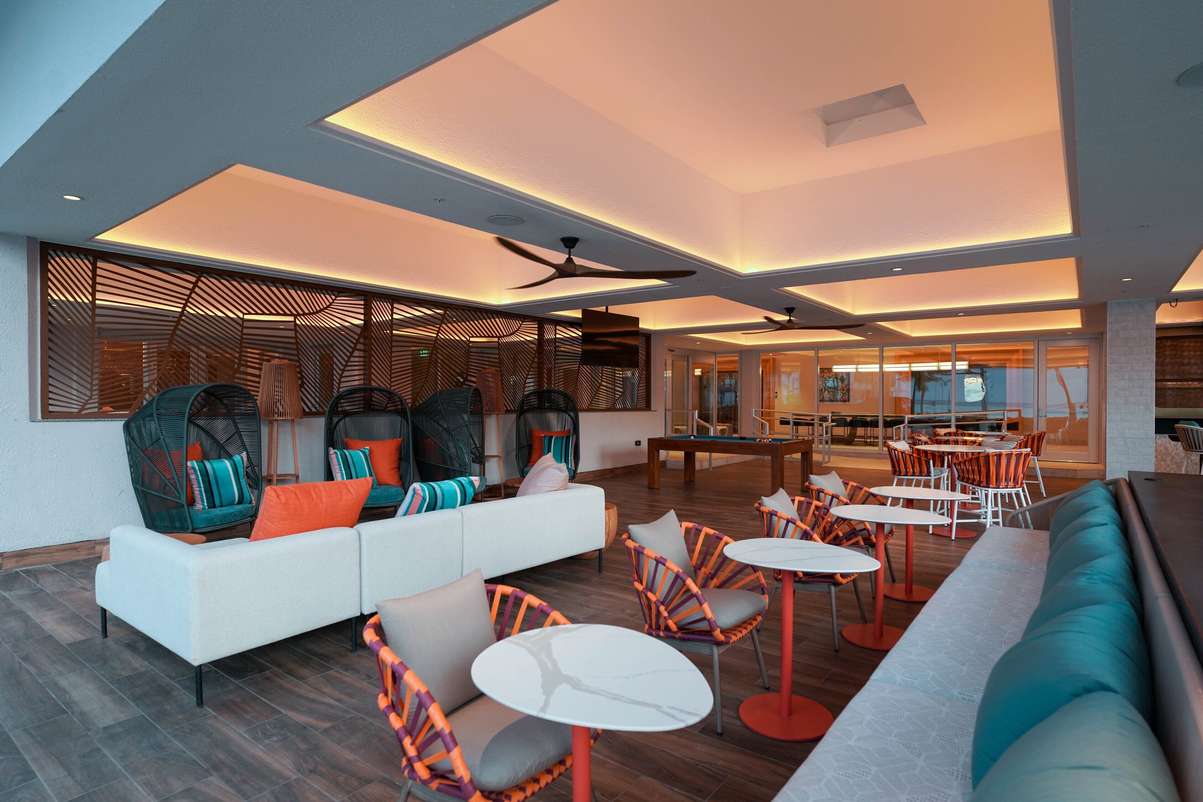 A modern lounge area with a sofa, chairs, and tables, featuring a ceiling fan and recessed lighting.