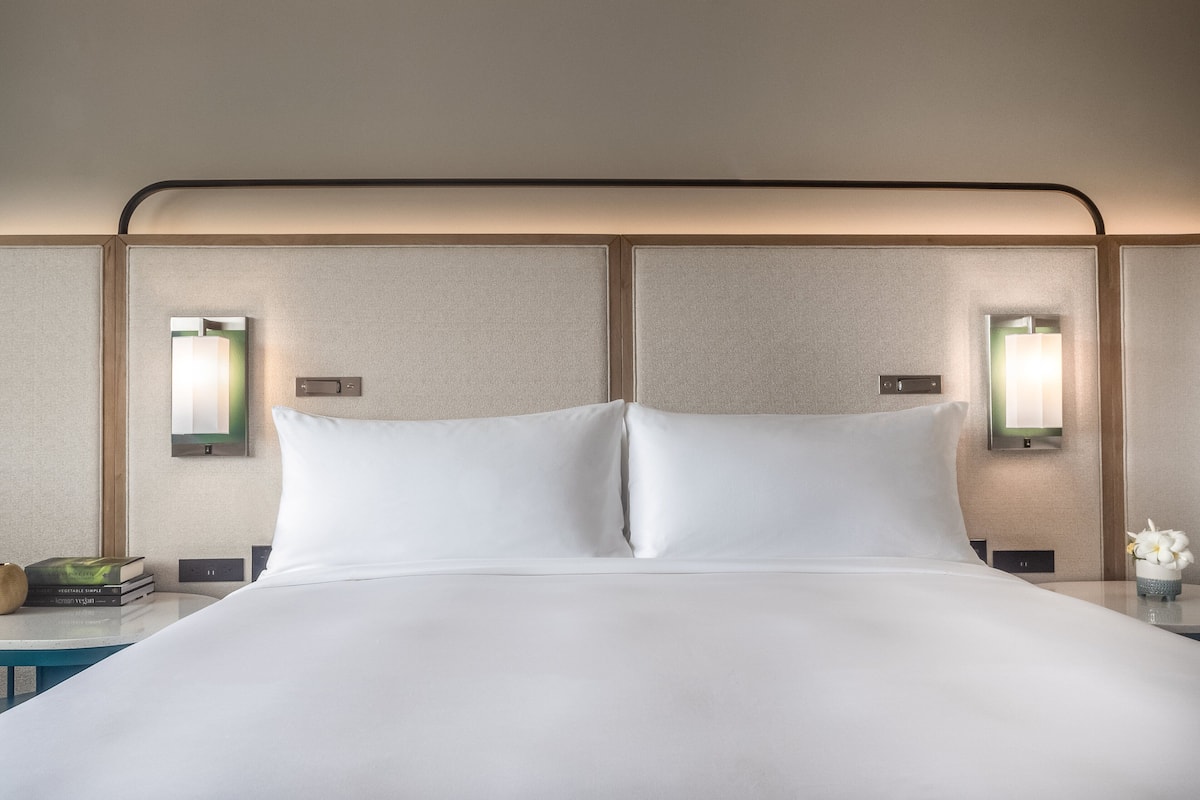 A neatly made bed with white linens, two bedside tables with lamps, and a small vase with flowers on one table.