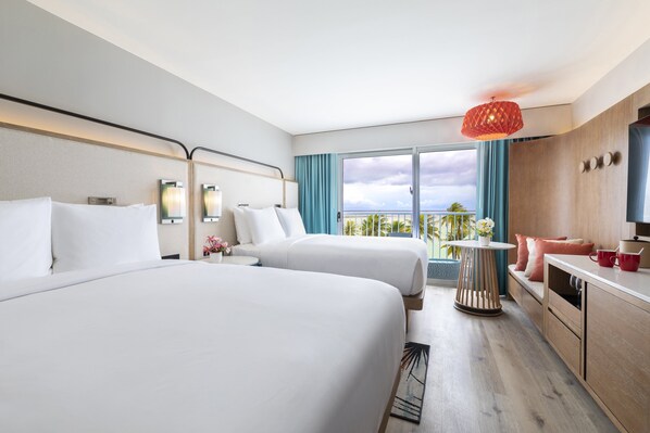 Habitación de hotel con dos camas, una mesita, un sofá y vista al océano.