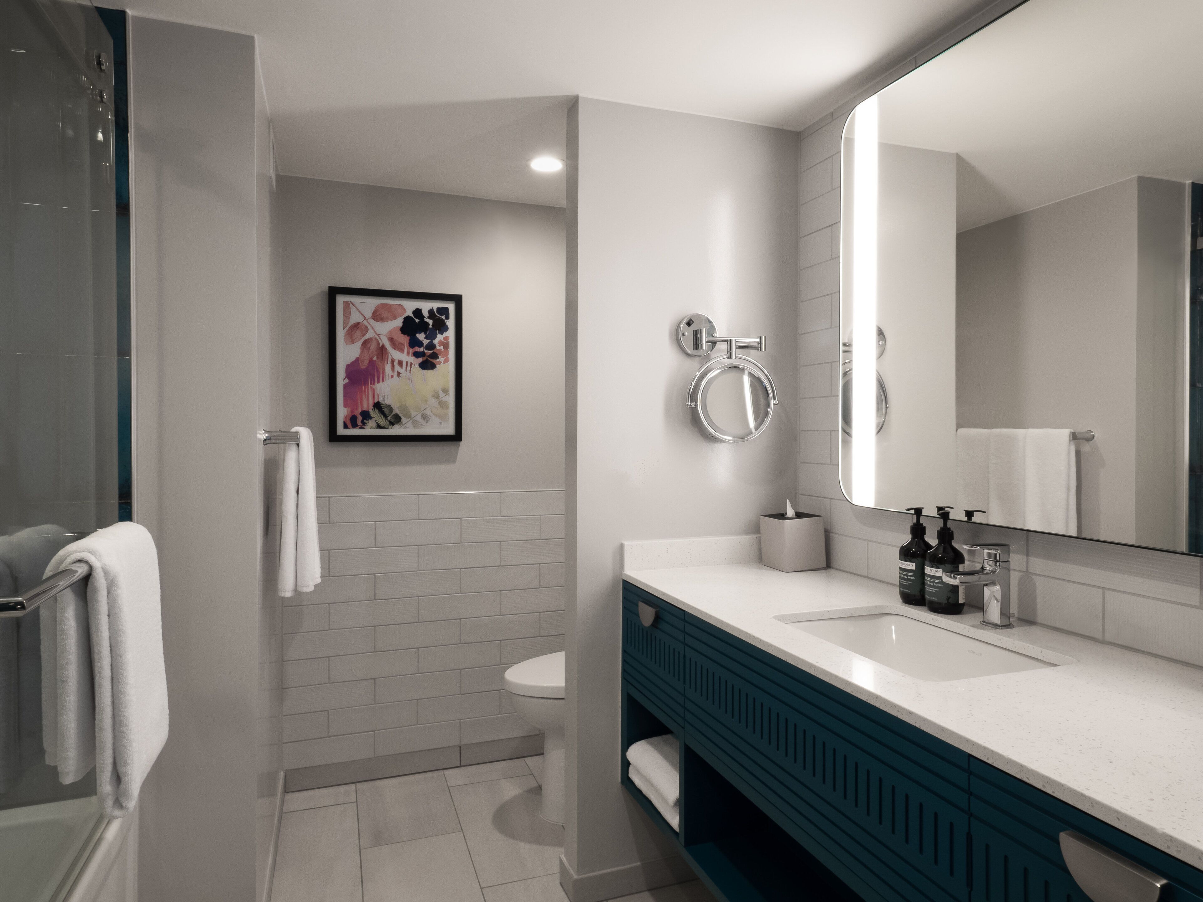 A modern bathroom with a white toilet, a large mirror, a sink with a white countertop, and a shower area.