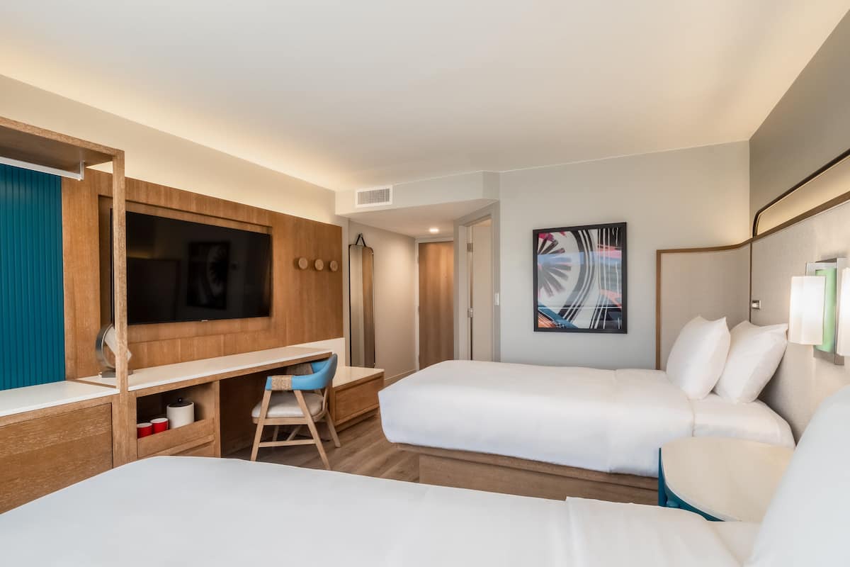 A hotel room with two beds, a desk, a chair, a TV, and a bathroom door.