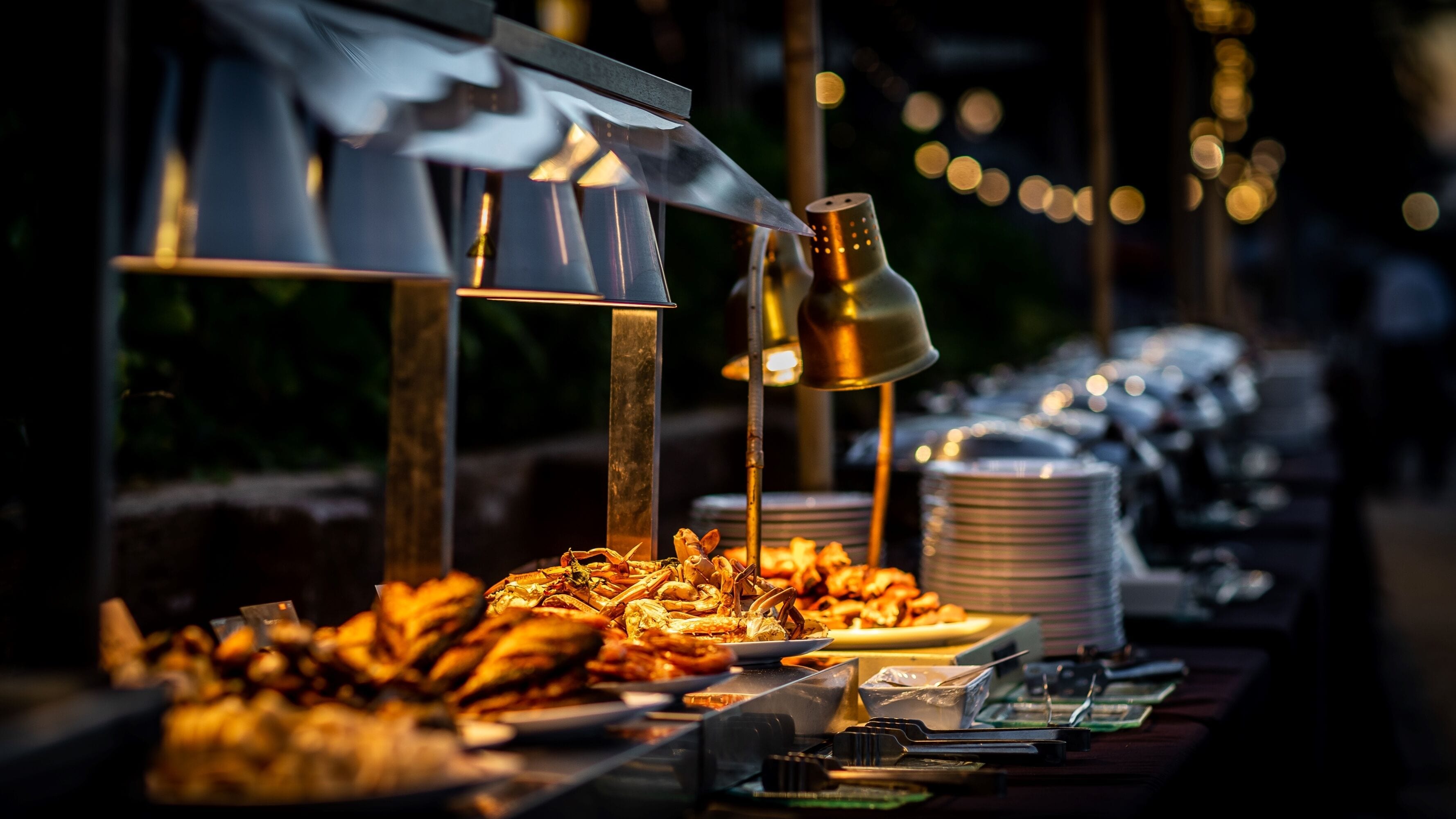 A buffet setup with seafood dishes, a stack of white plates, and a buffet trolleys.
