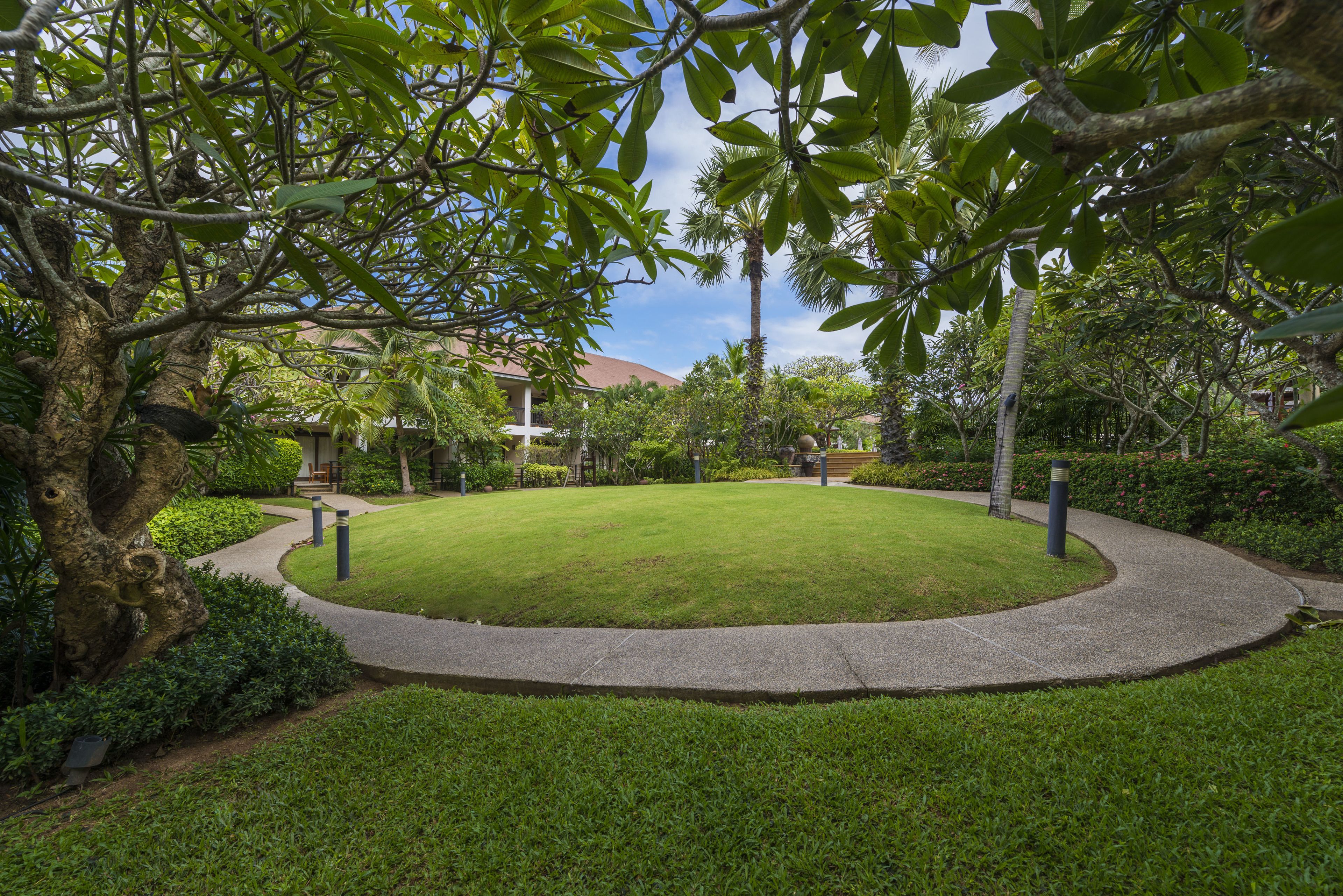 A well-maintained garden with a circular lawn, a curved pathway, and a building in the background.