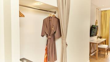A hotel room with a robe hanging on a rack, a wooden chair, a small table, and a television on the wall.