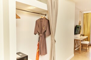 A hotel room with a robe hanging on a rack, a wooden chair, a small table, and a television on the wall.