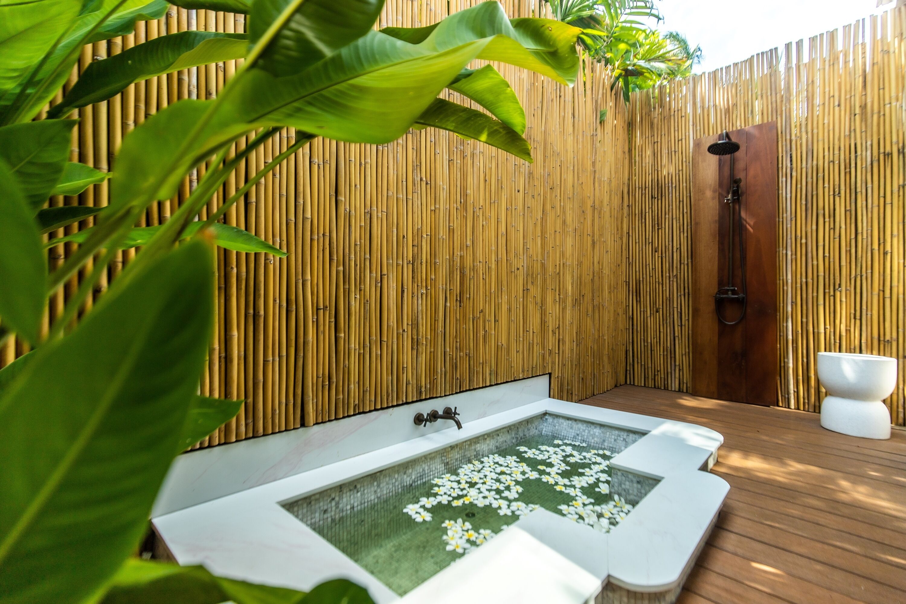 A spa area with a wooden deck, a hot tub with flowers, and a bamboo wall.