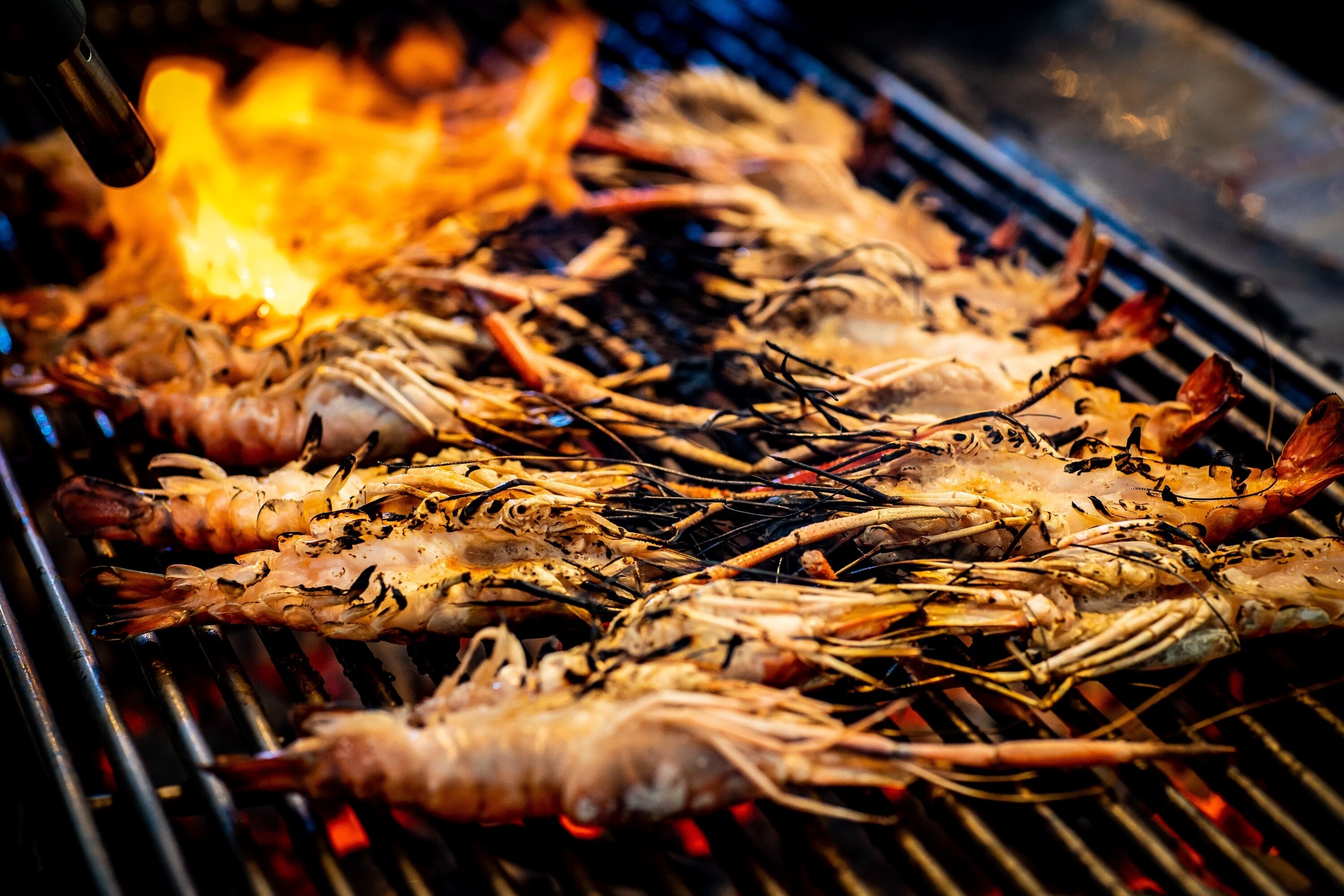 Grilled prawns on a grill with visible flames.