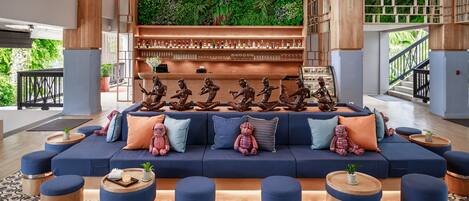 A modern lounge area with a blue sofa, wooden ottomans, and a green wall with plants.