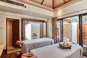 A spa room with two massage tables, a stone wall, and a view of a garden.