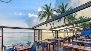 Un área de comedor al aire libre con mesas y sillas, con vista a una playa y al mar.
