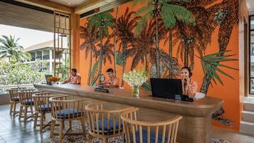 A reception area with a wooden reception desk, several wooden chairs with blue cushions, and a large mural of palm trees on the wall.