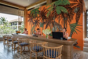A reception area with a wooden reception desk, several wooden chairs with blue cushions, and a large mural of palm trees on the wall.