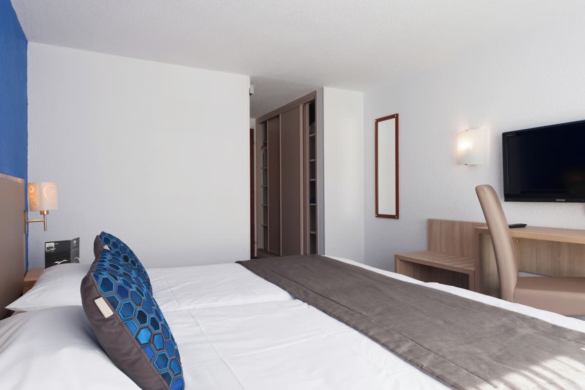Une chambre d’hôtel équipée d’un lit, d’un bureau, d’une chaise, d’une télévision et d’une armoire.