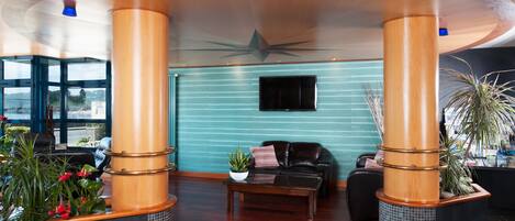 A lobby with wooden pillars, a teal wall, a flat-screen TV, a coffee table, and a seating area with a couch and chairs.