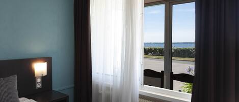 A hotel room with a bed, a nightstand with a lamp, a window with curtains, and a view of the outside.