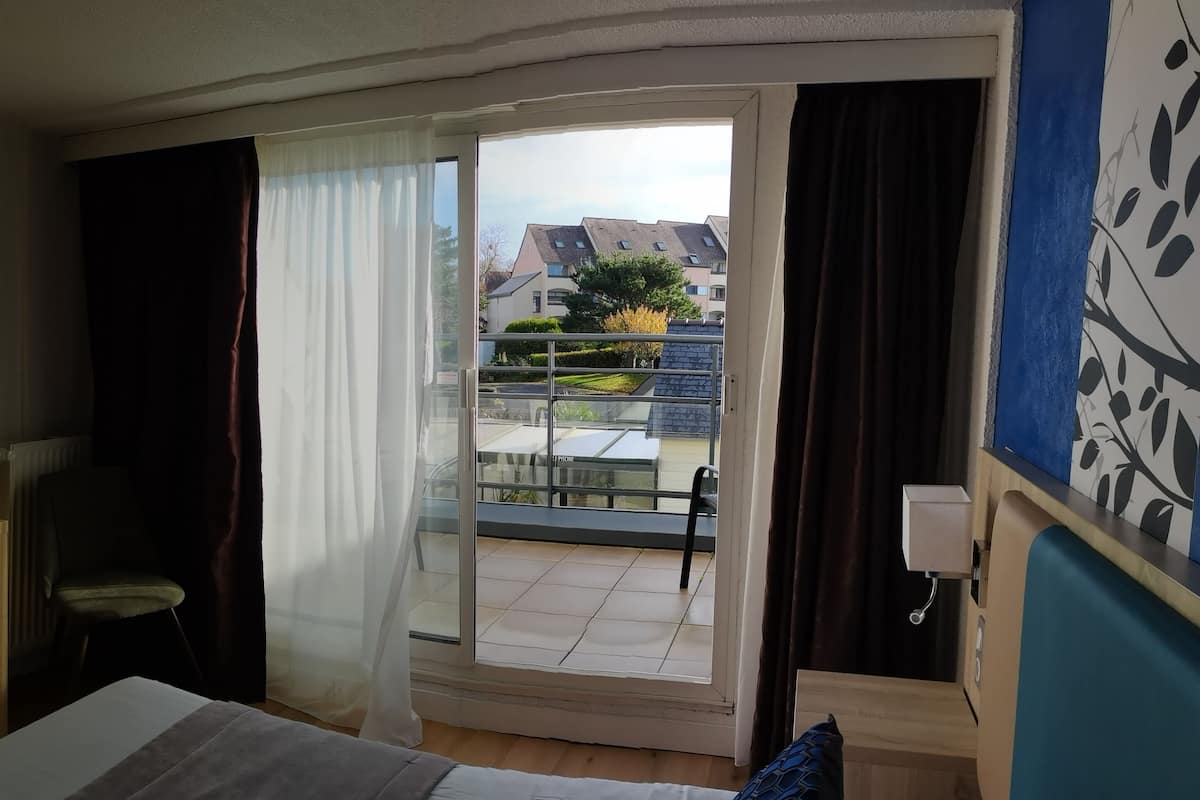Une chambre d’hôtel comprenant un lit, un bureau, une chaise, une télévision, une fenêtre avec des rideaux et une vue sur le balcon extérieur.