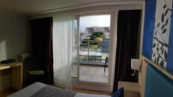 A hotel room with a bed, a desk, a chair, a TV, a window with curtains, and a view of the outside balcony area.