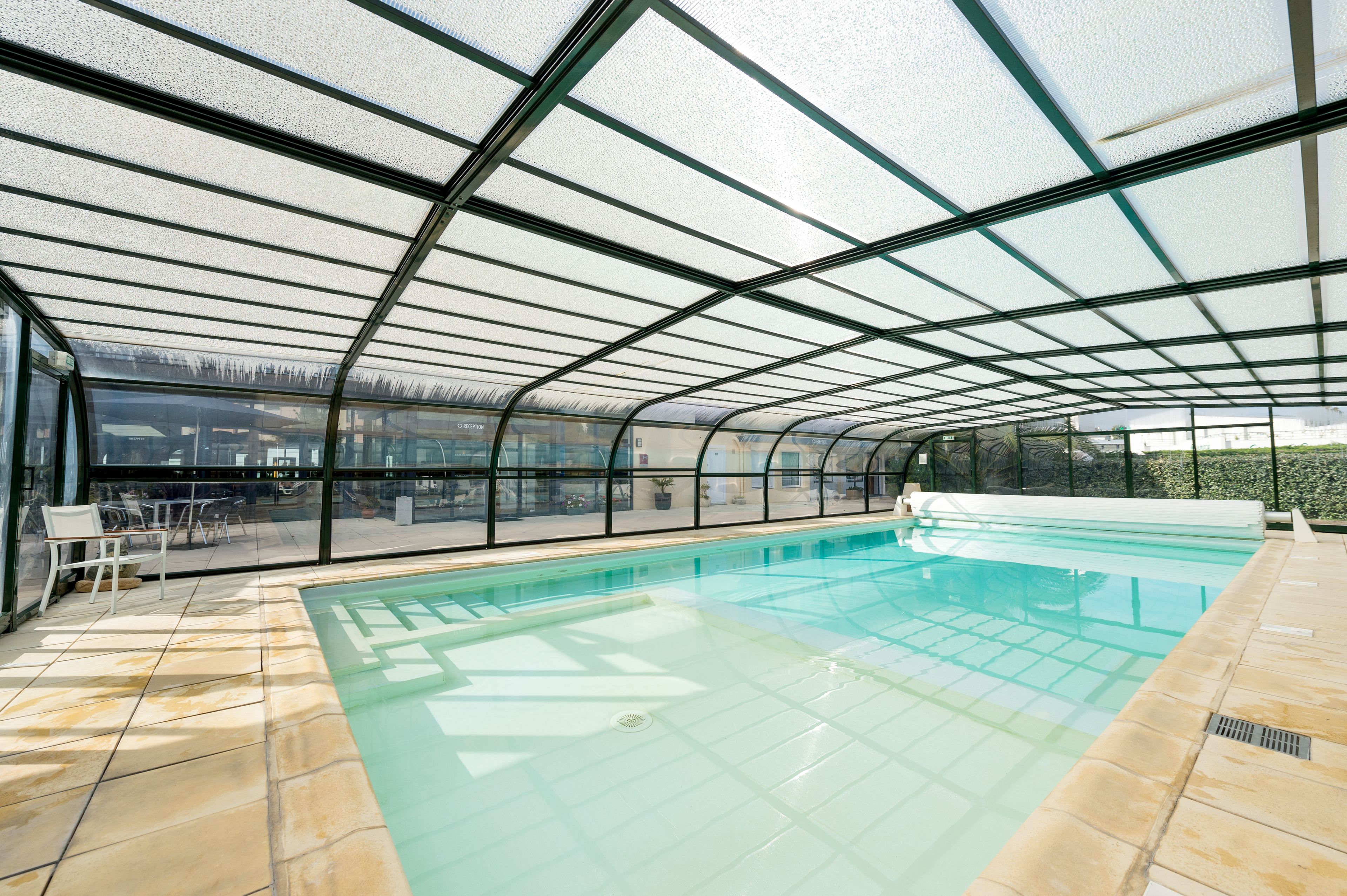 An indoor swimming pool with a glass ceiling, tiled floor, and a view of the outdoors.