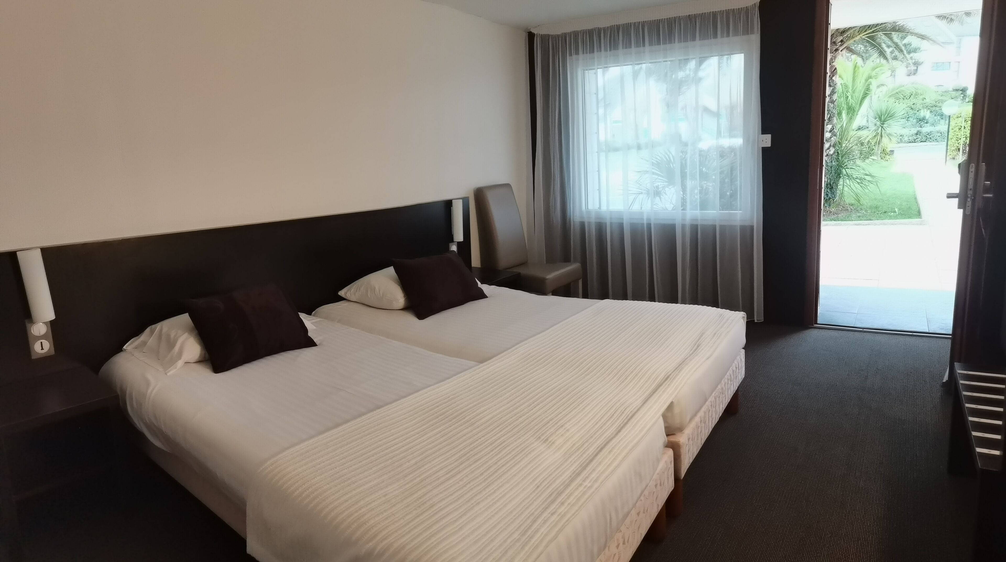 Habitación de hotel con una cama grande, dos mesitas de noche, una silla y una ventana con cortinas.