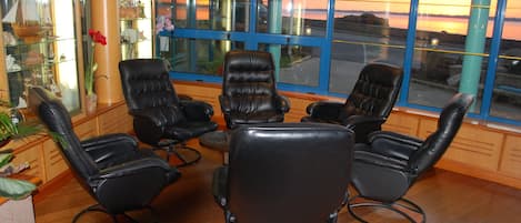 A room with a view of a sunset over water, featuring black leather chairs arranged around a small table.