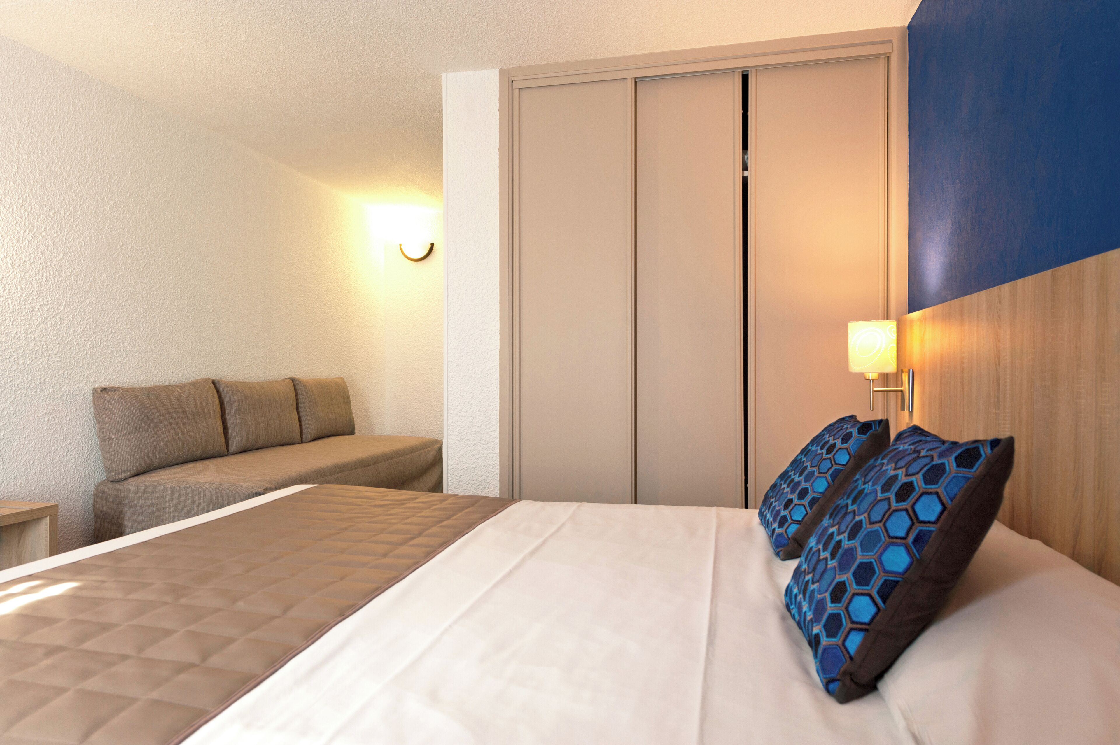 Una habitación de hotel con una cama, un sofá, una mesita de noche y una lámpara fijada a la pared.