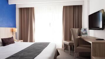 Een hotelkamer met een bed, een bureau, een stoel, een televisie en gordijnen.