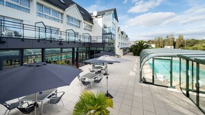 A hotel patio with outdoor seating, a swimming pool, and a glass-enclosed area. - Hôtel de l’Océan Concarneau (Concarneau)