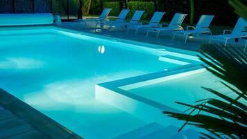 Piscina com água azul cristalina, rodeada por espreguiçadeiras e palmeiras.