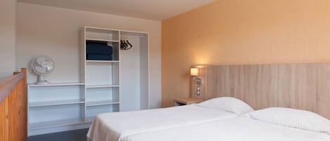 A hotel room with two beds, a wardrobe, a bedside table with a lamp, and a ceiling fan.