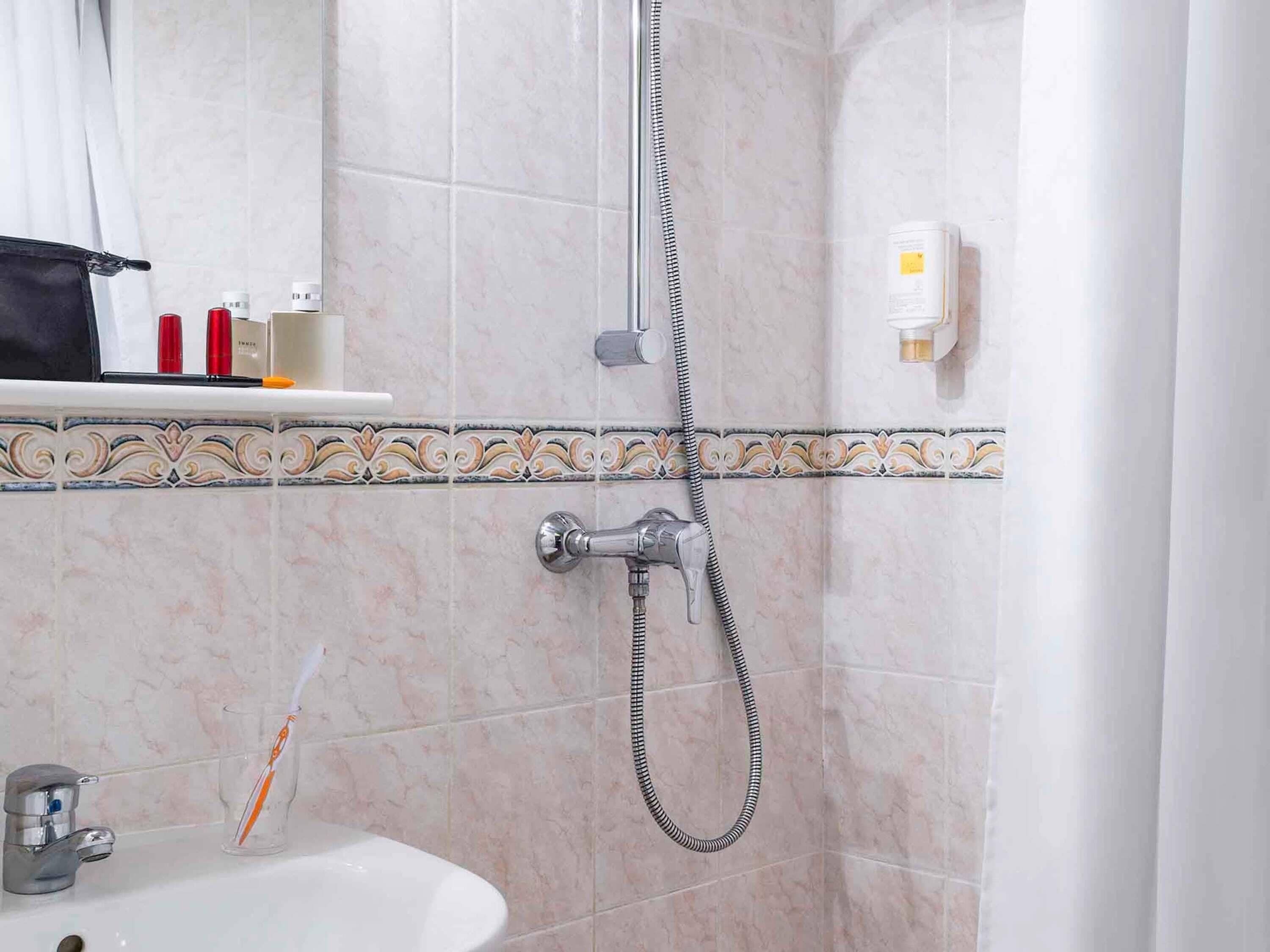 Un baño con ducha, lavabo y artículos de aseo en un estante.