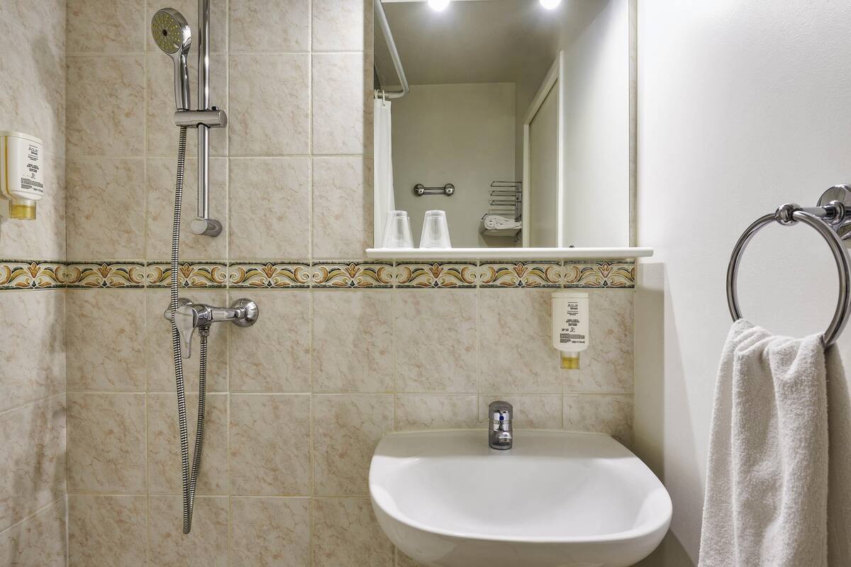 A bathroom with a shower, sink, mirror, towel rack, and toiletries.