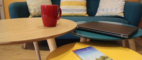 A round wooden table with a red mug, a laptop, and a brochure on a yellow surface.