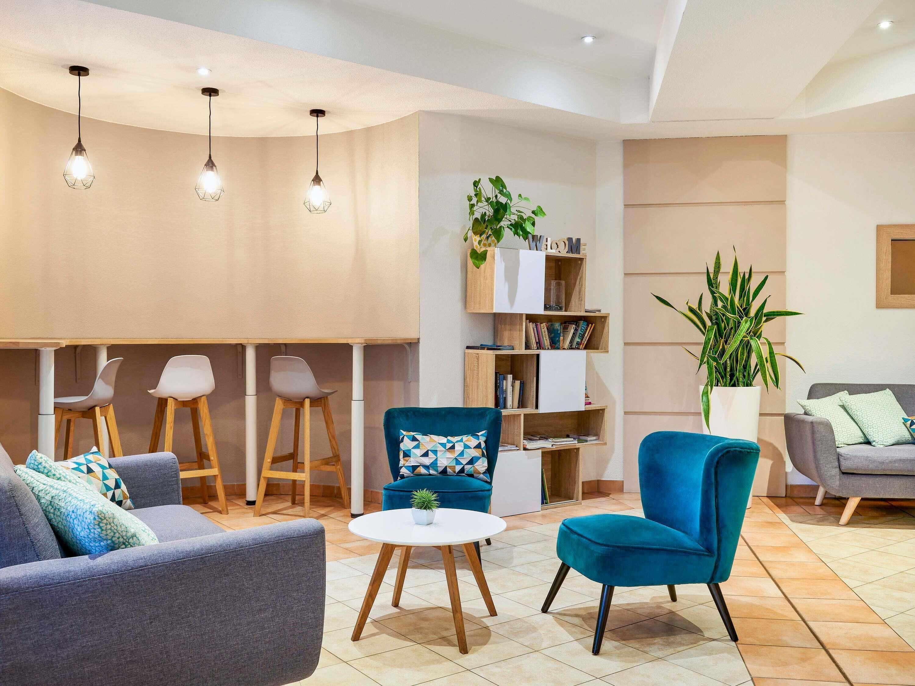 A modern living room with a sofa, armchairs, a small round table, and a bookshelf.