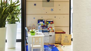 Un espace de jeux pour enfants avec une chaise blanche, un tapis bleu, des jouets éducatifs et un mur décoré d’étoiles et d’une tête de cerf.
