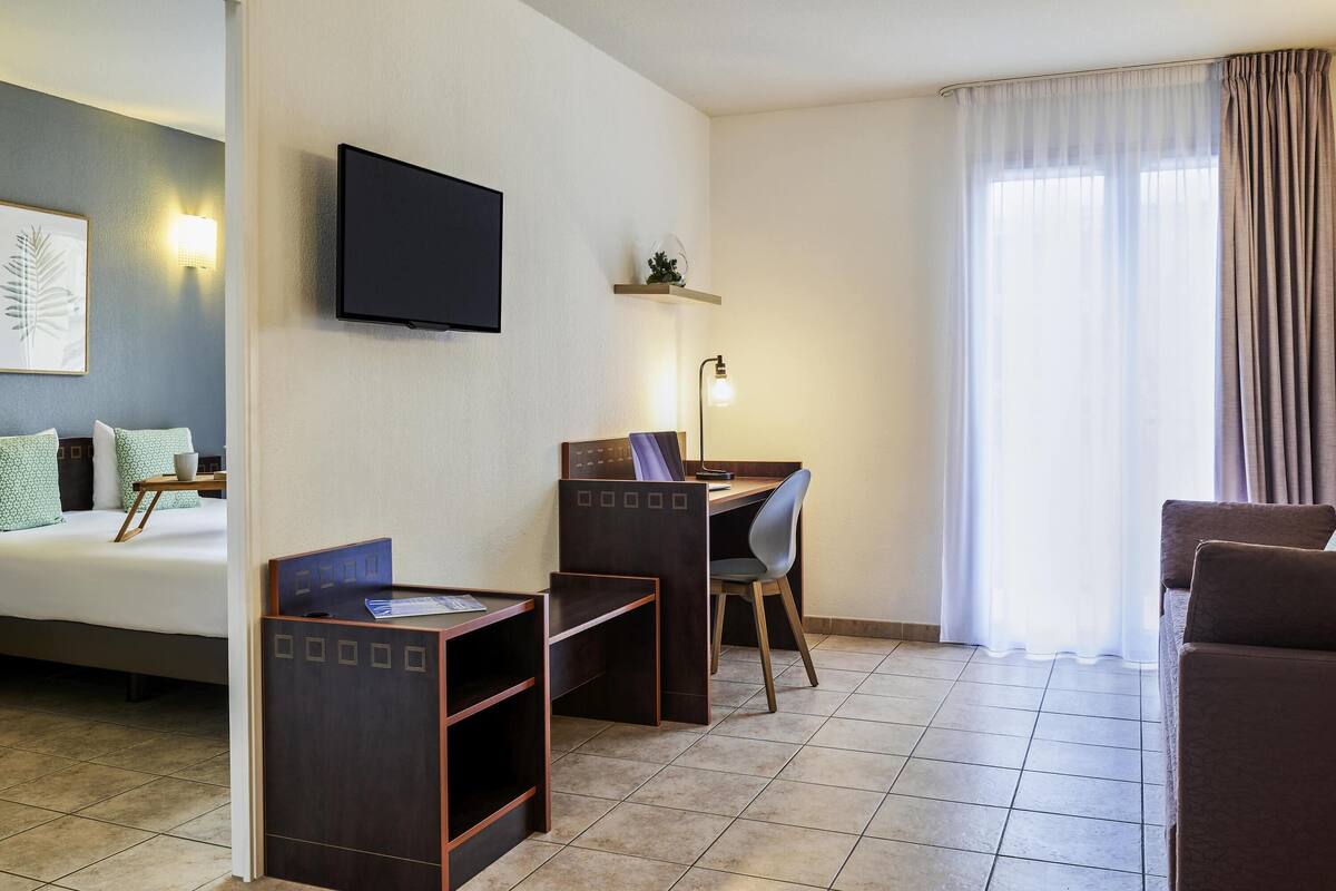 A hotel room with a bed, a desk with a chair, a television, and a window with curtains.