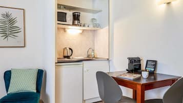 Cocina compacta equipada con microondas, cafetera y lavavajillas. Cuenta con una mesa de comedor con dos sillas y una silla azul verdoso.