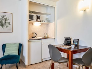 A compact kitchen with a microwave, coffee maker, and a dishwasher. There is a dining table with two chairs and a teal chair. - Aparthotel Adagio Access Nice Garibaldi (Nice)