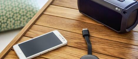 A smartphone, a black speaker, and a charging cable on a wooden tray.