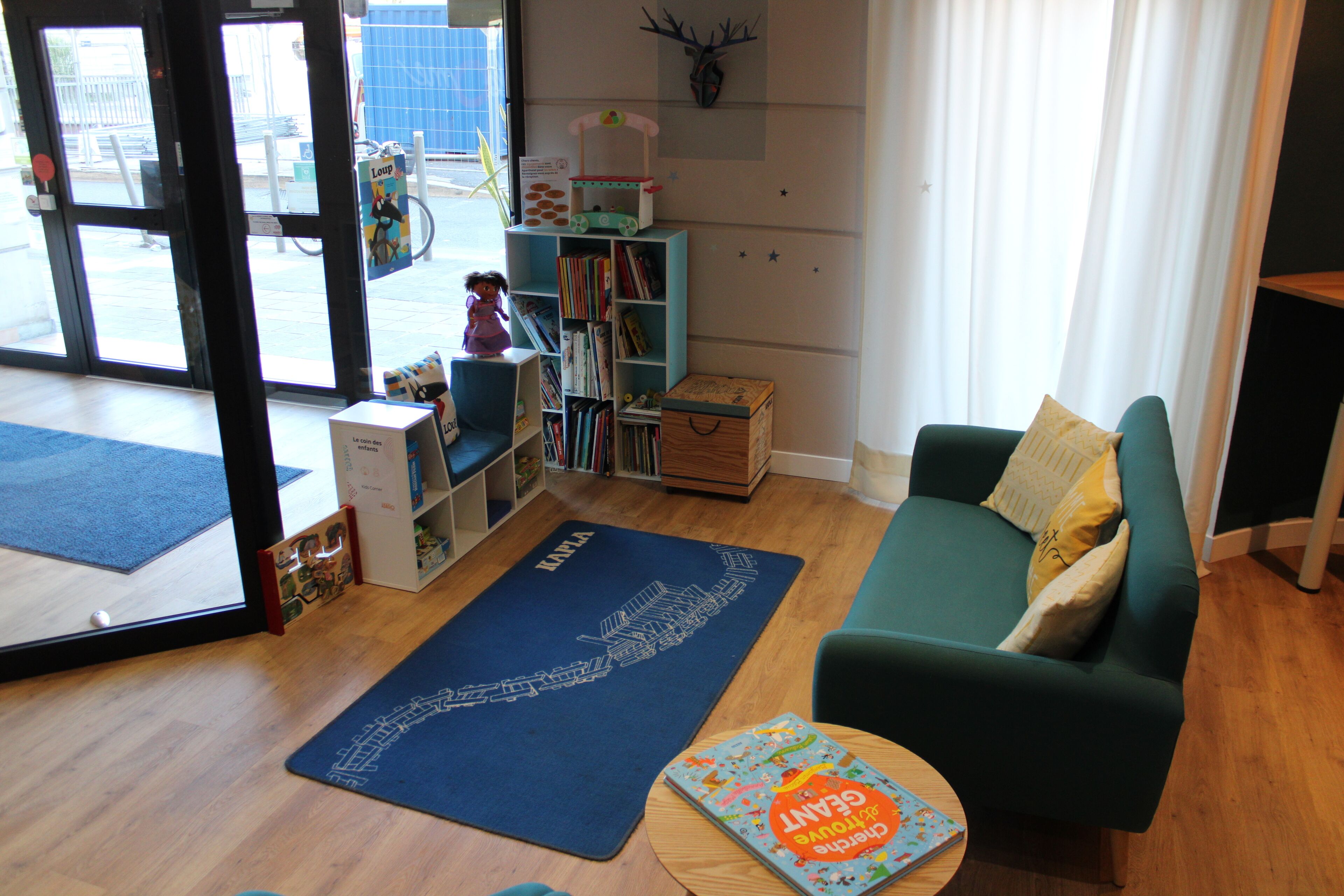 Ein gemütliches Wohnzimmer mit einem grünen Sofa, einem blauen Teppich und einem Bücherregal voller Bücher.
