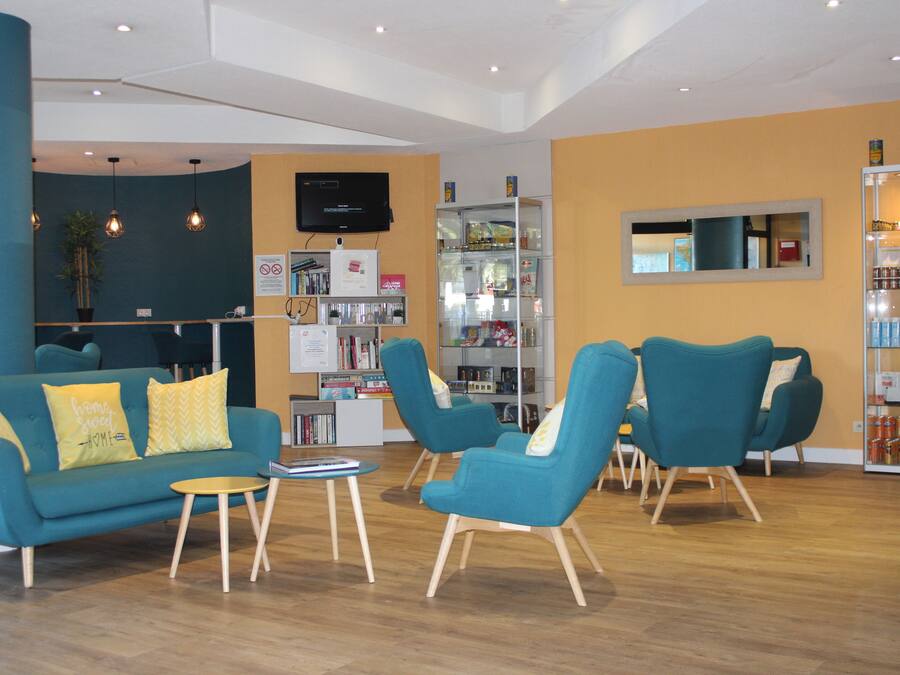 A modern lounge area with teal sofas, a coffee table, and a bookshelf.