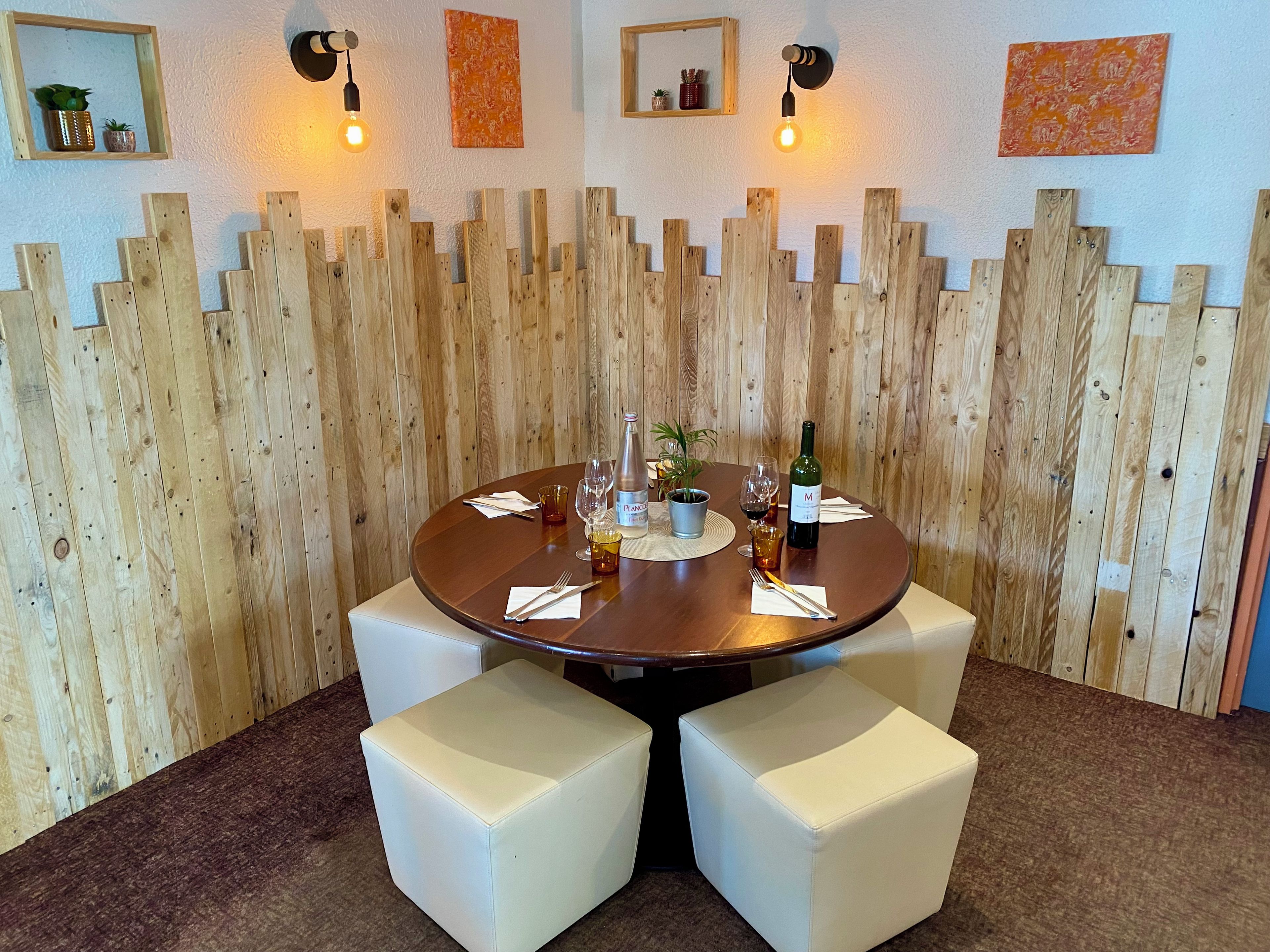 Una mesa redonda con cuatro asientos blancos acolchados, una botella de vino y copas sobre una pared de madera con diseño de panel vertical.