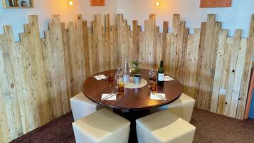 Una mesa redonda con cuatro asientos blancos acolchados, una botella de vino y copas sobre una pared de madera con diseño de panel vertical.