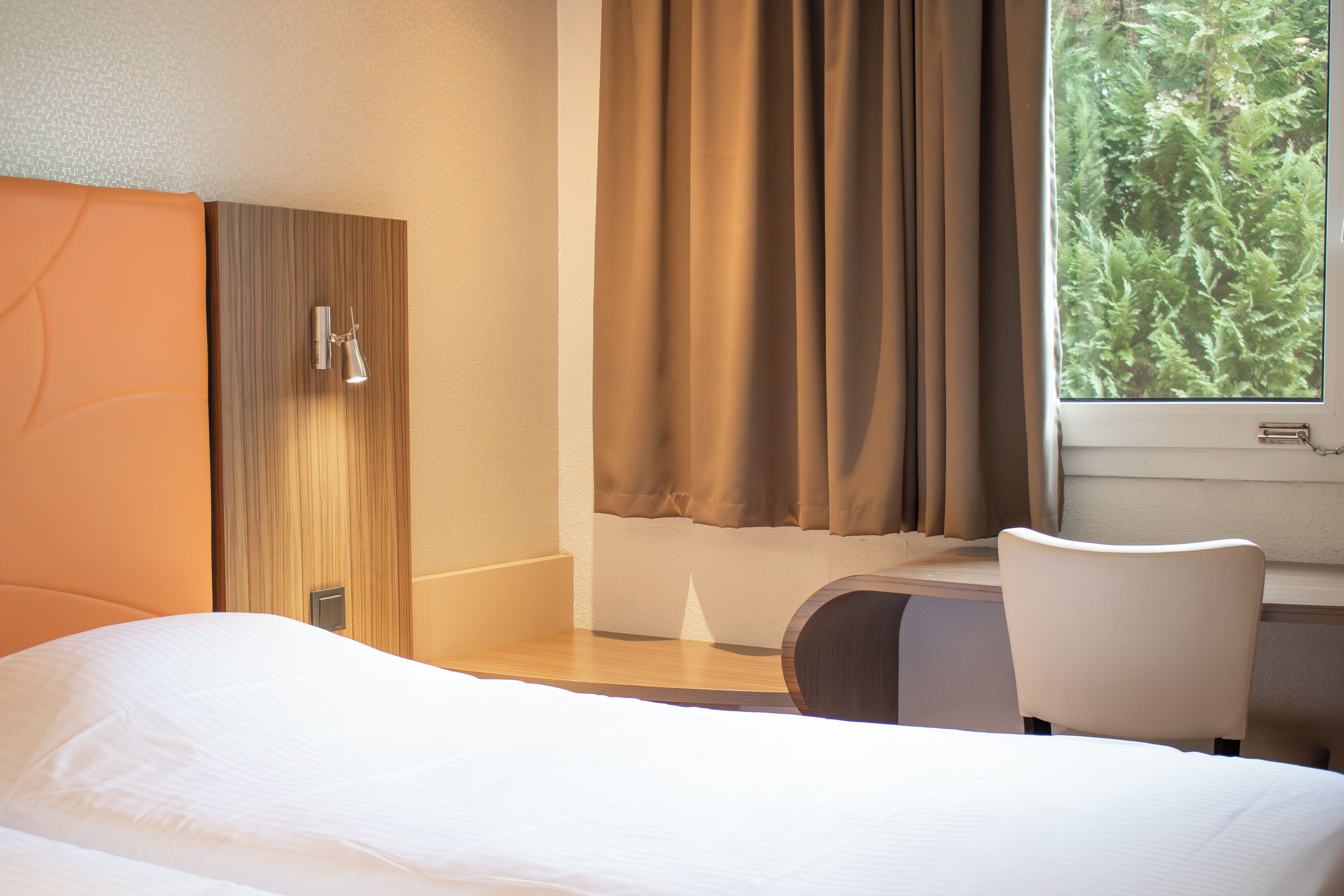 Une chambre d’hôtel avec un lit, une chaise, une fenêtre avec des rideaux et une vue sur la verdure.