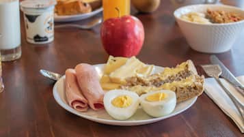 Ontbijt bord met ham, eieren, brood, een glas sinaasappelsap en een rode appel op een houten tafel.