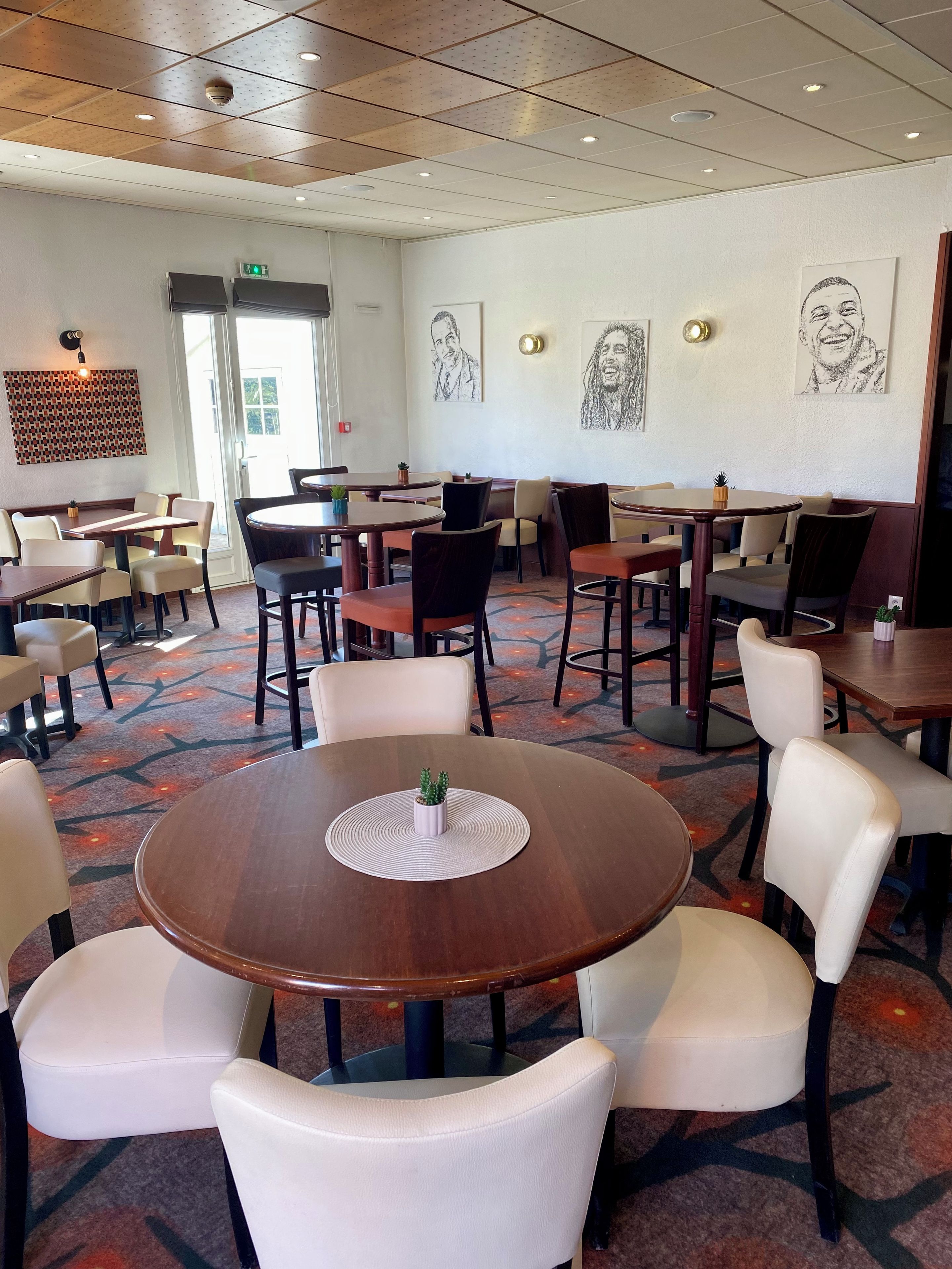 Un espace de restauration d’hôtel avec des tables rondes, des chaises et des œuvres d’art murales.