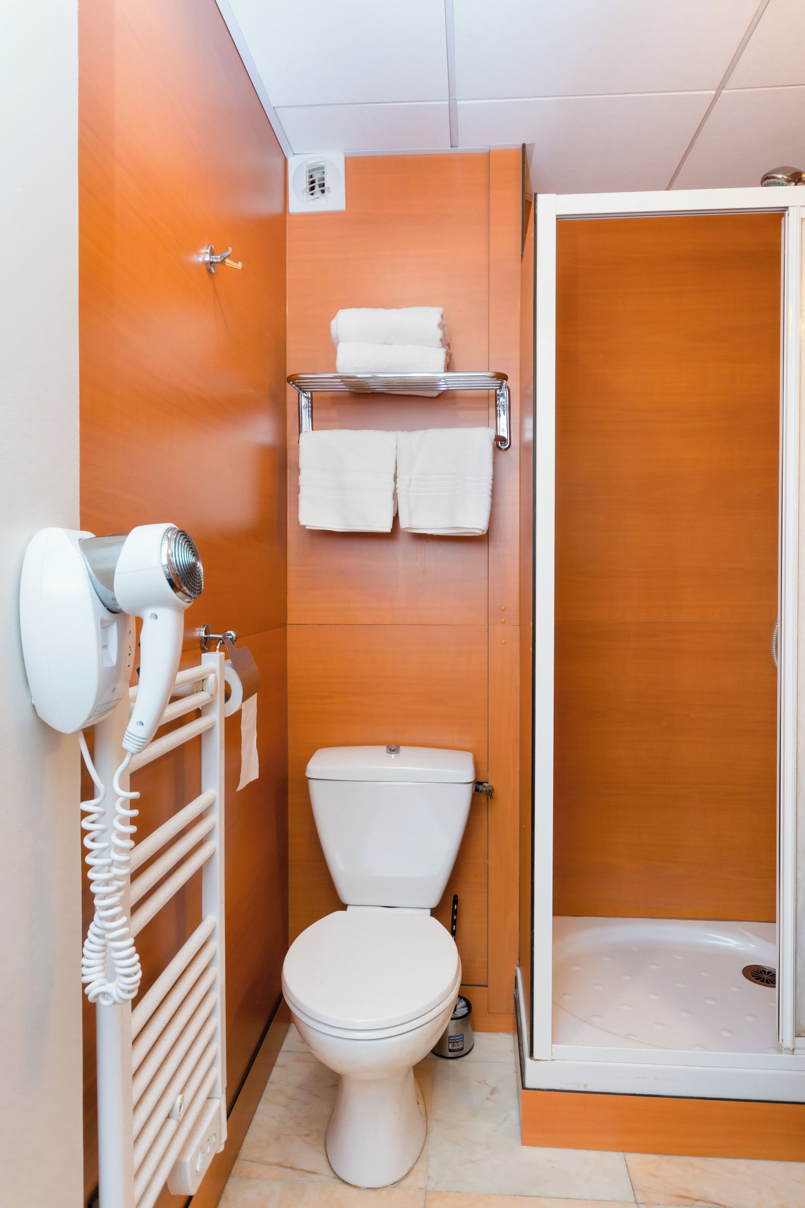 Un baño con inodoro blanco, secador de pelo, toallero y cabina de ducha.