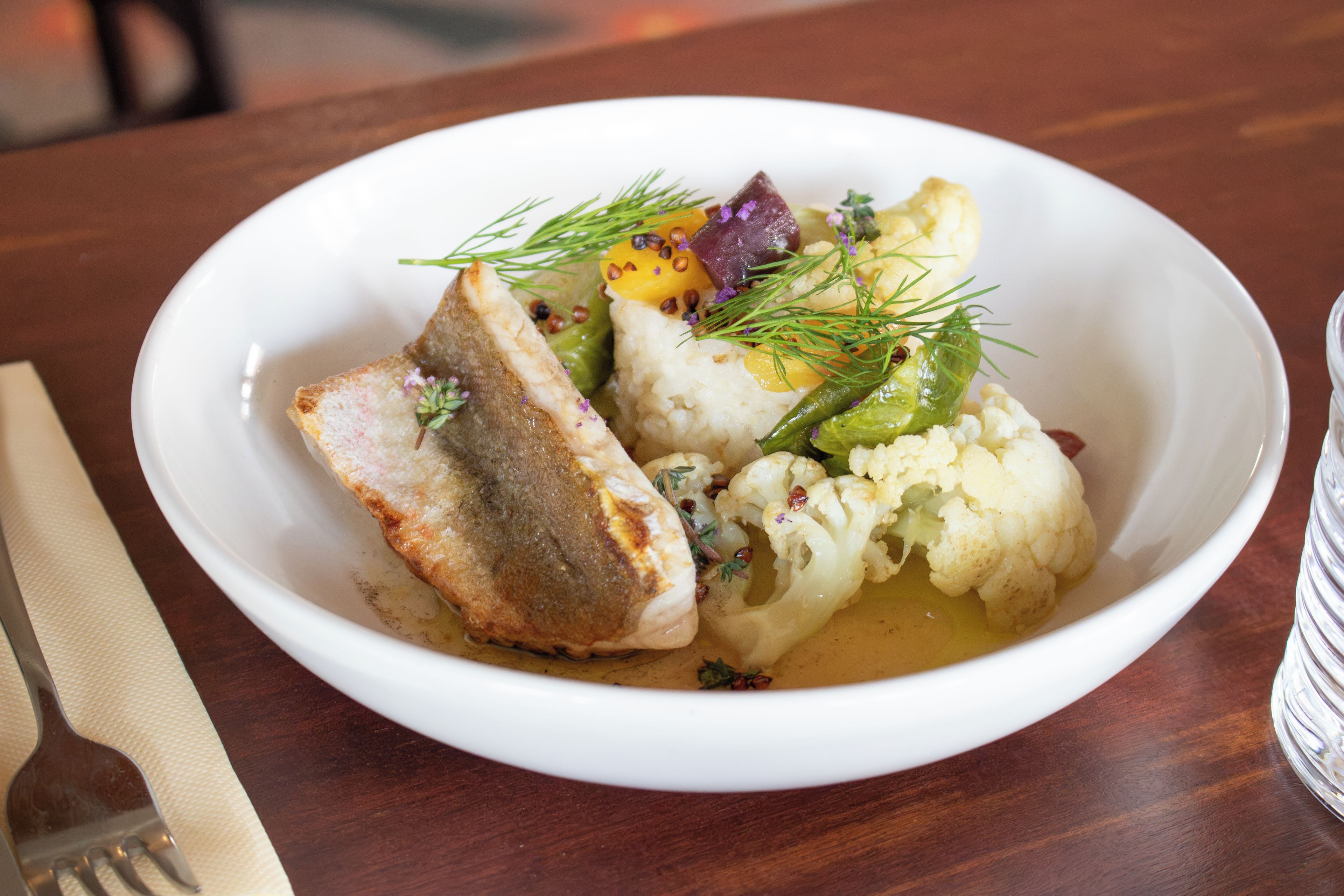 Un plato blanco con pan, puré de papas, coliflor y una guarnición de eneldo y flores moradas.
