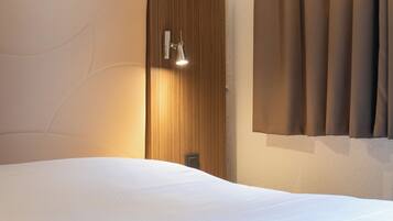 Una habitación de hotel con una cama grande, cabecera de madera, lámpara de pared y una ventana con cortinas.
