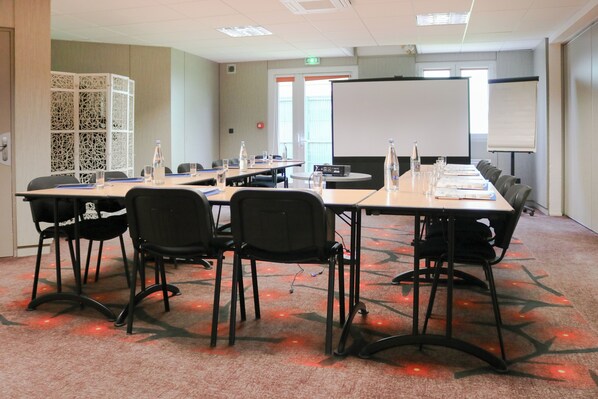 Un salón de conferencias con una larga mesa, sillas, una pizarra y una pantalla de proyector.
