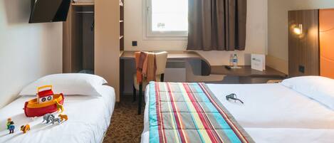 Quarto de hotel com duas camas, uma escrivaninha, televisão fixada na parede e uma janela com cortinas.